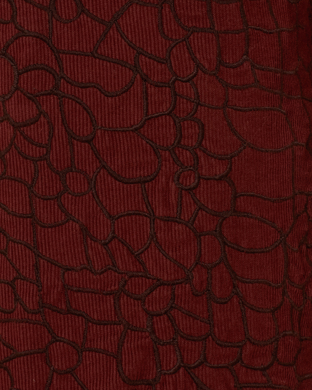 Close-up of the Cooper Auburn Crocodile Pant’s textured, dark red corduroy fabric featuring an irregular black-outlined pattern that evokes abstract shapes or a crocodile-skin motif—perfect for making a statement.