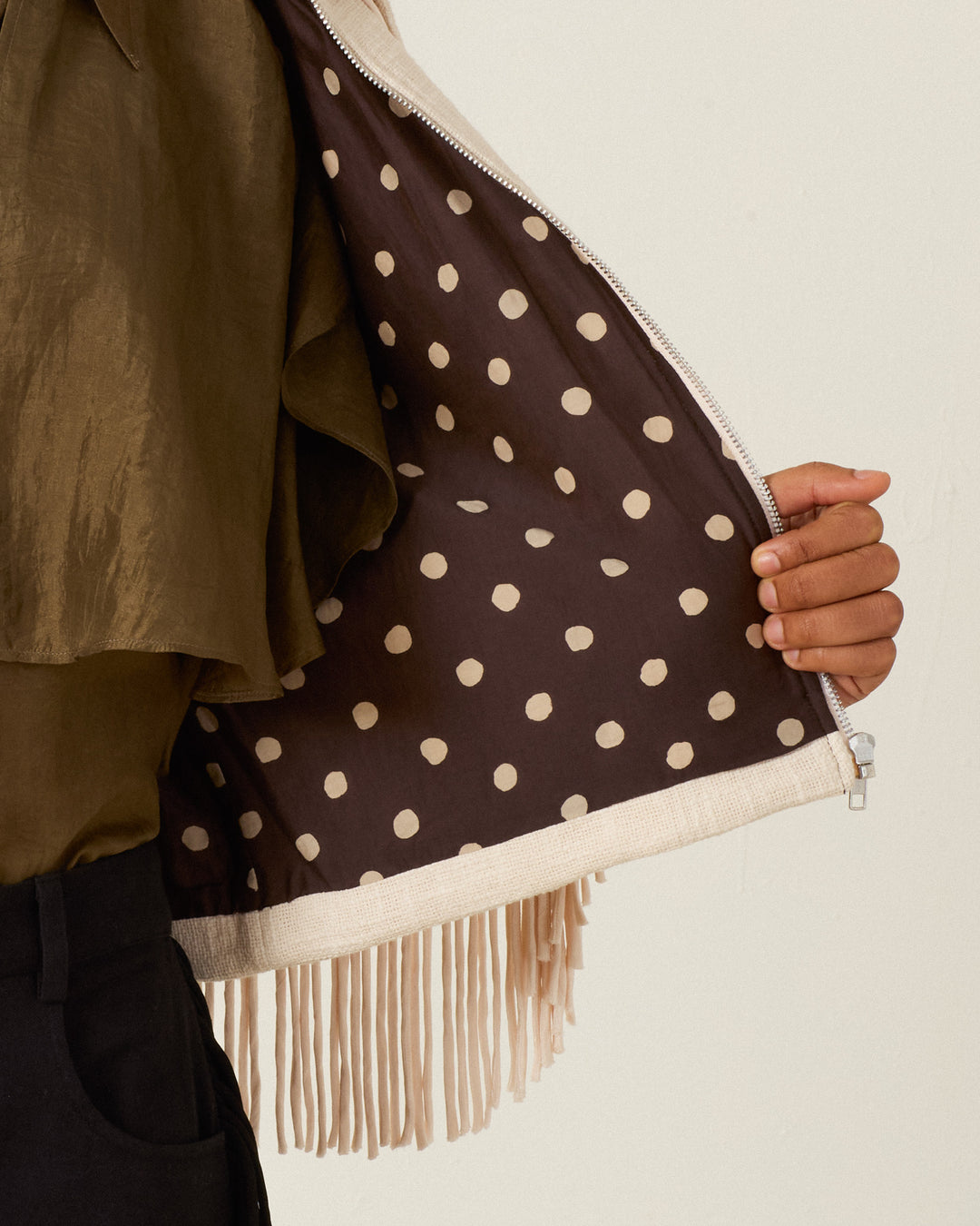A person opens the Court Prairie Fringe Jacket, revealing its brown and beige polka dot lining and Western-inspired fringing.