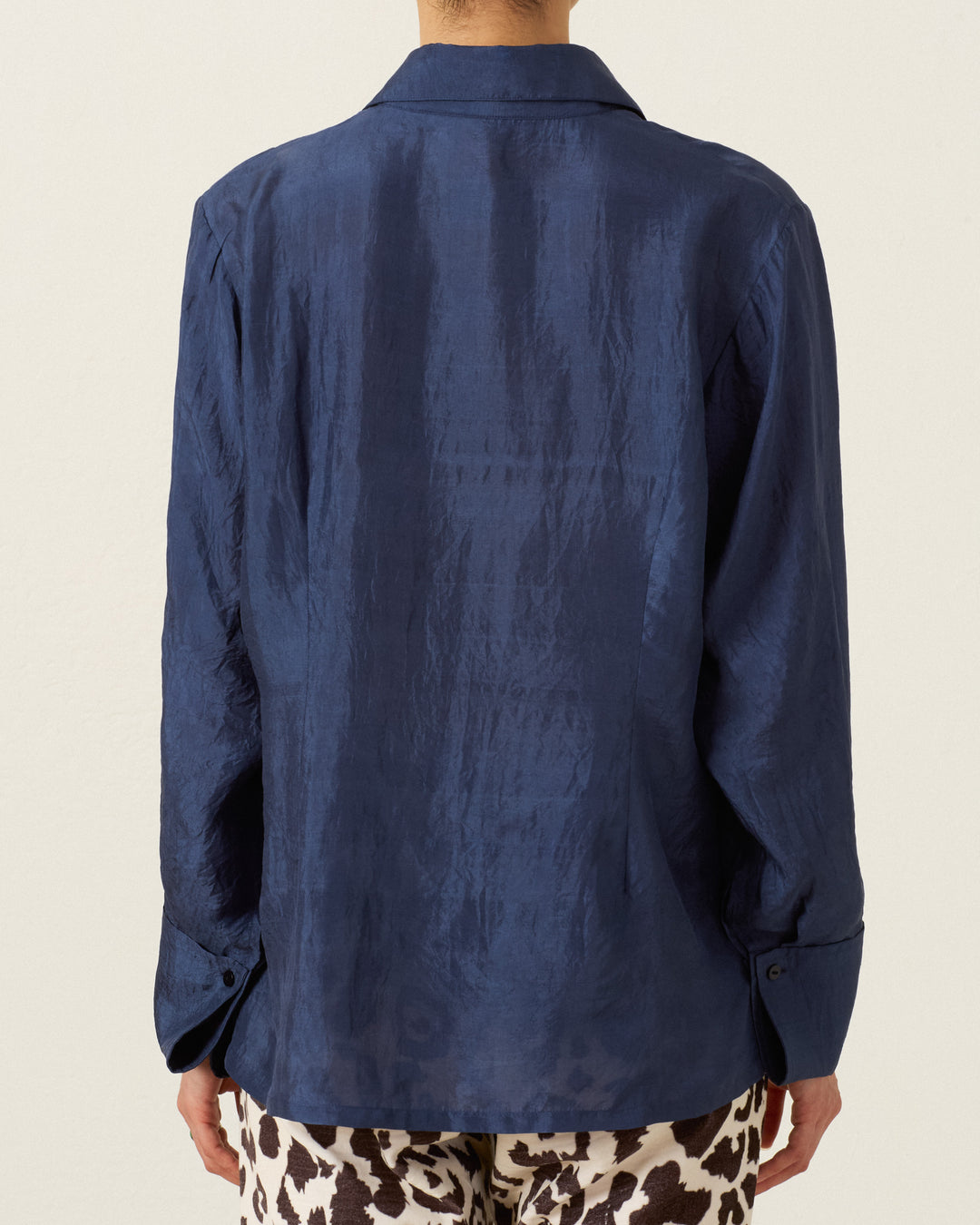 A person is seen from the back wearing the Dana Indigo Night Silk Shirt, a long-sleeve, navy blue hand-loomed silk button-up with a lustrous finish, paired with patterned brown and white pants.