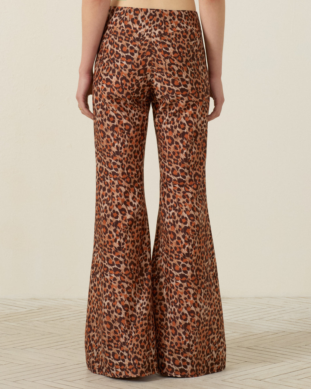 Person standing with their back to the camera, wearing the Farah Leopard Trek Pant—high-waisted, bell-bottom flare pants with a bold brown and black leopard print pattern.