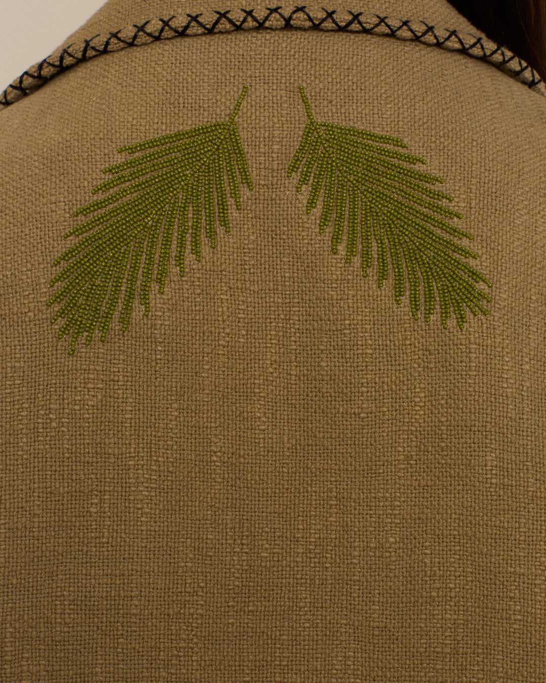 Close-up of the Francis Heron Rider Jacket in beige Khadi cotton, featuring two green embroidered leaf motifs and black decorative stitching along the top edge.