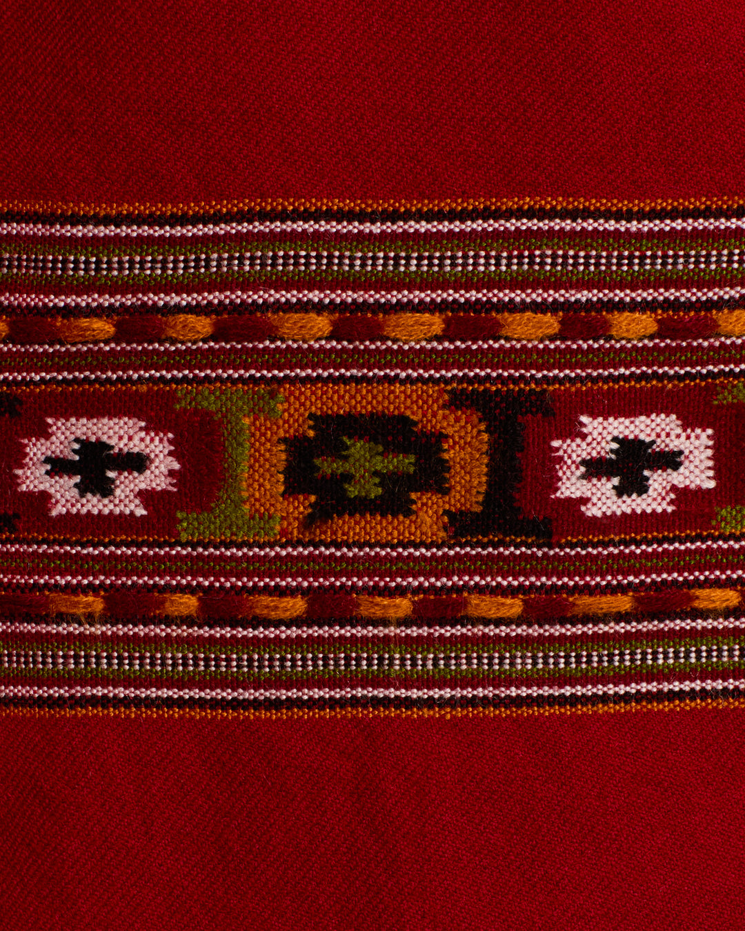 The Grace Chili Tree Wool Coat features a vivid red textile adorned with horizontal woven bands in green, white, yellow, and brown geometric patterns and motifs; its decorative stripes showcase intricate craftsmanship inspired by Himalayan artisan garment traditions.