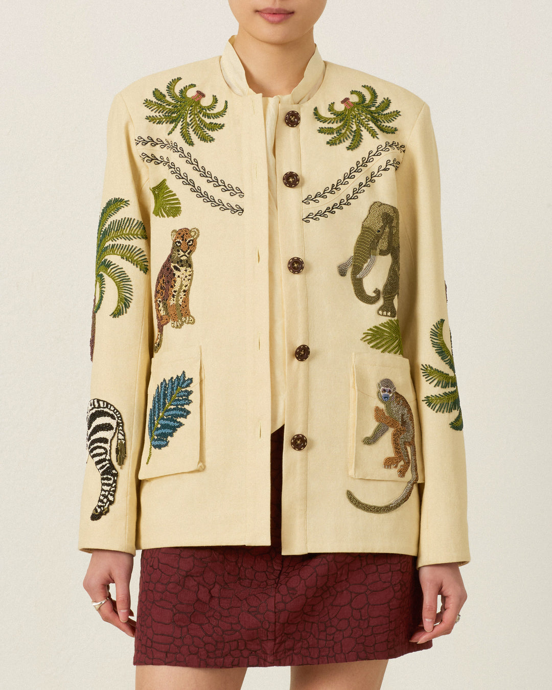Wearing the Judson Jungle Book Jacket—a safari-inspired cream piece featuring embroidered animals and leaves—paired with a burgundy skirt.