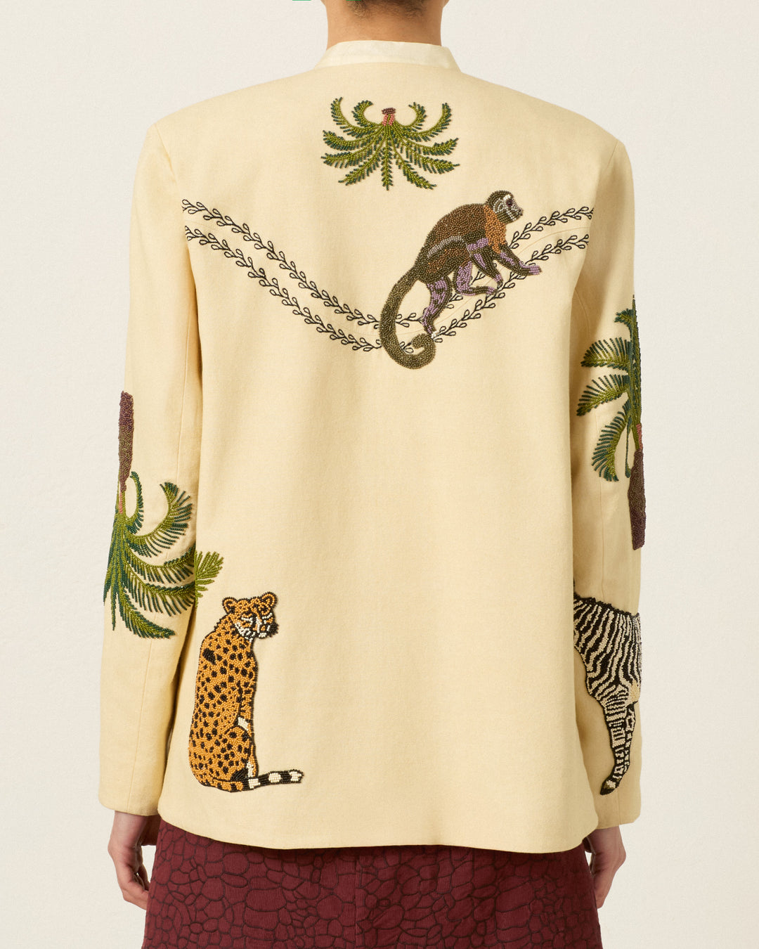 Wearing the Judson Jungle Book Jacket—a safari-inspired cream jacket adorned on the back with embroidered animals and trees, including a monkey, cheetah, and zebra.