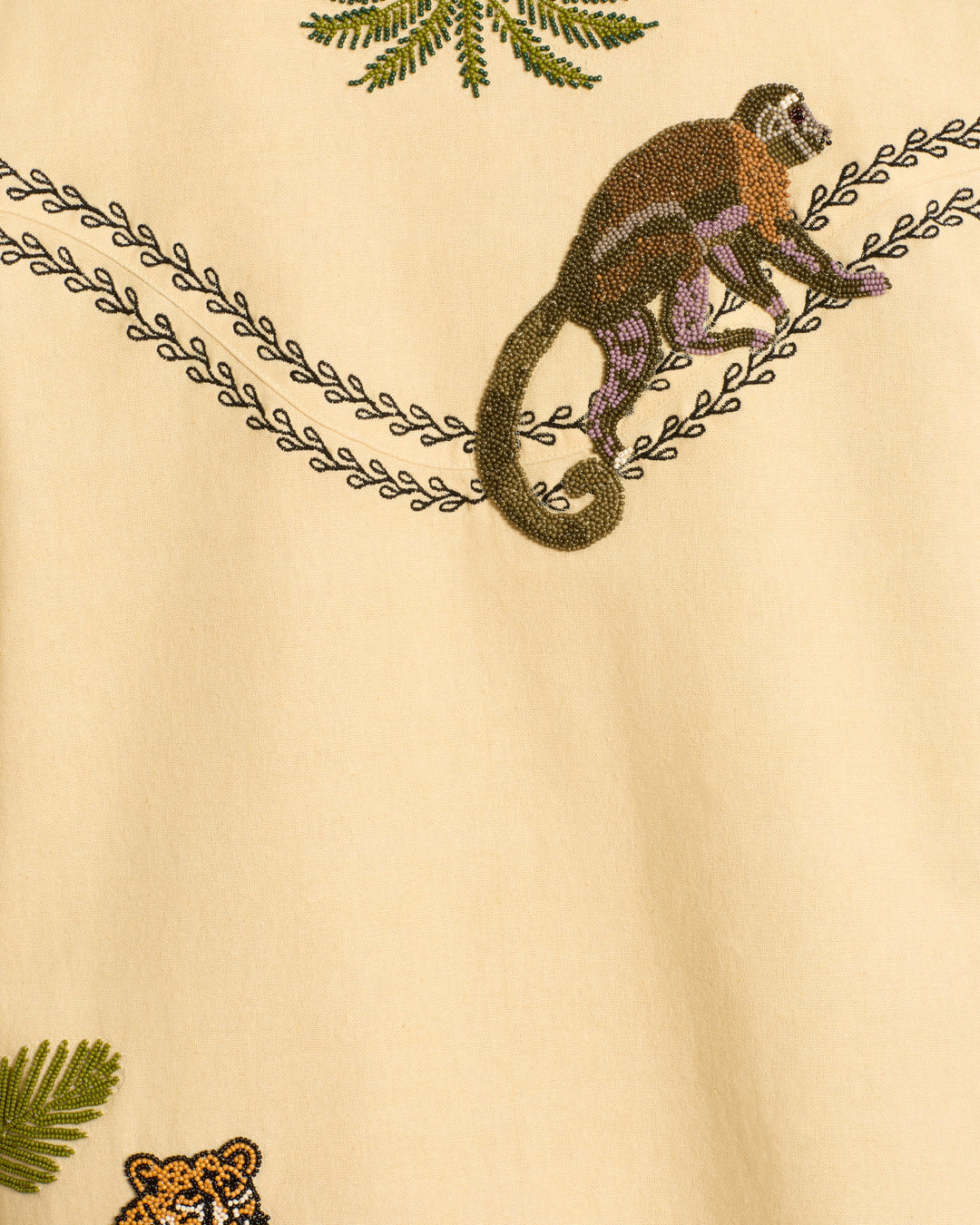 The Judson Jungle Book Jacket features an embroidered monkey sitting on a branch with leafy accents on beige fabric, complemented by a partial tiger face and leaves for a safari-inspired, embellished look.