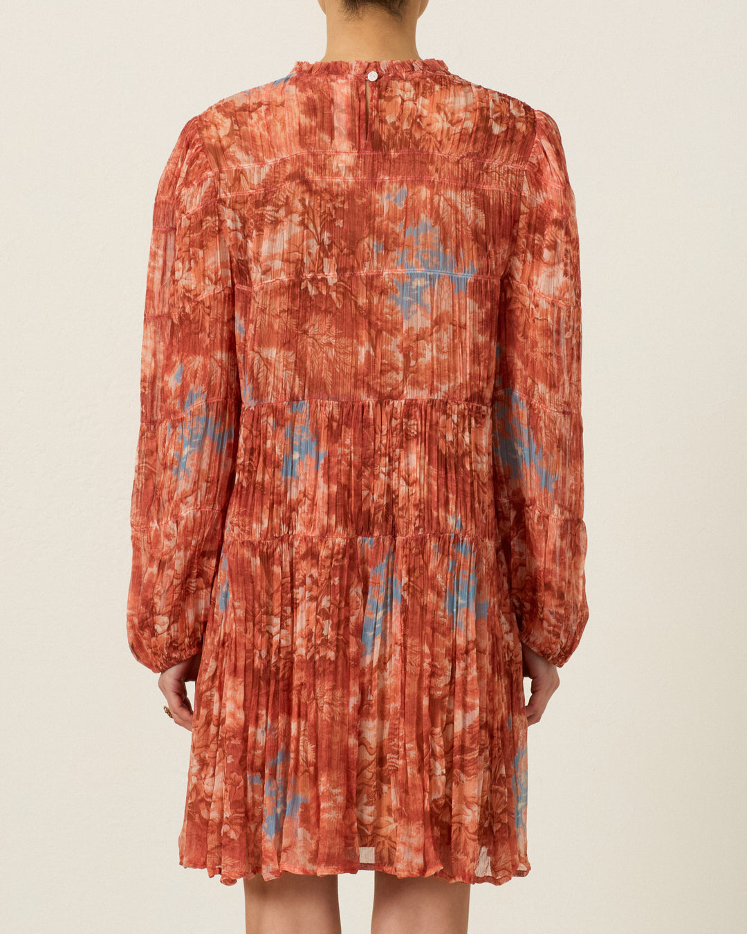 A person shown from the back wearing the Juno Heritage Canopy Dress, a long-sleeved, knee-length pleated dress featuring a red and blue abstract pattern and a ruffle-trimmed neckline.