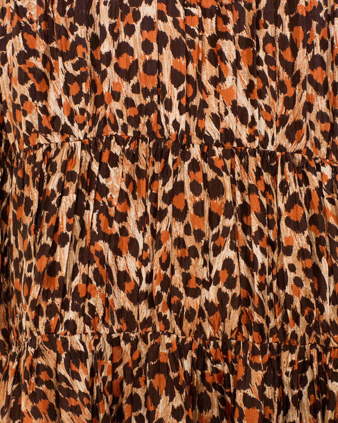 Close-up of gathered or ruffled horizontal seams on the Juno Leopard Trek Silk Dress, showcasing its hand-loomed silk fabric in a chic mini silhouette with a leopard print pattern in shades of brown, black, and tan.
