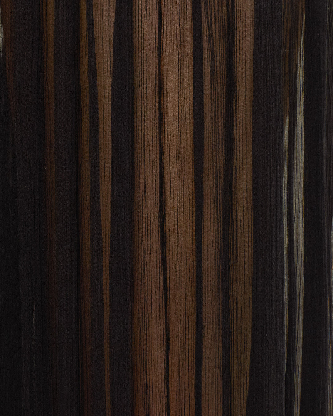 Close-up of the Keats Onyx Chiffon Pant’s dark wood-inspired surface, featuring vertical stripes and natural grain patterns in varying shades of brown and black—reminiscent of flowing cupro-chiffon textures and the pleated detailing often seen on harem pants with an elasticated waist.