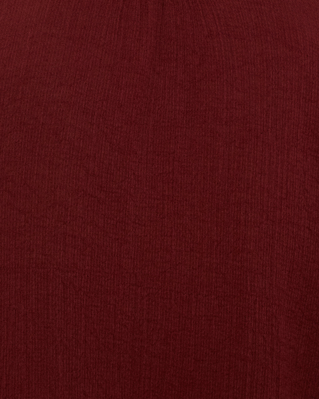 A close-up of the textured maroon fabric of the Kiki Mahogany Shirt, featuring visible vertical lines and subtle shading evocative of refined cotton dobby shirts in classic Edwardian silhouettes.
