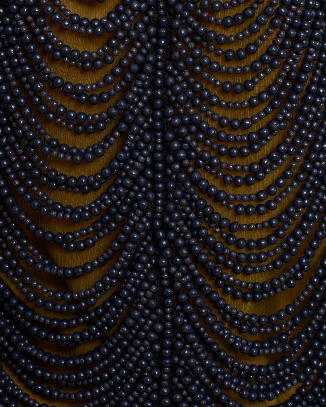 Multiple strands of black beads are draped in a symmetrical pattern against a wooden background, showcasing the intricate detail of the Lania Indigo Wooden Top handmade by artisans.