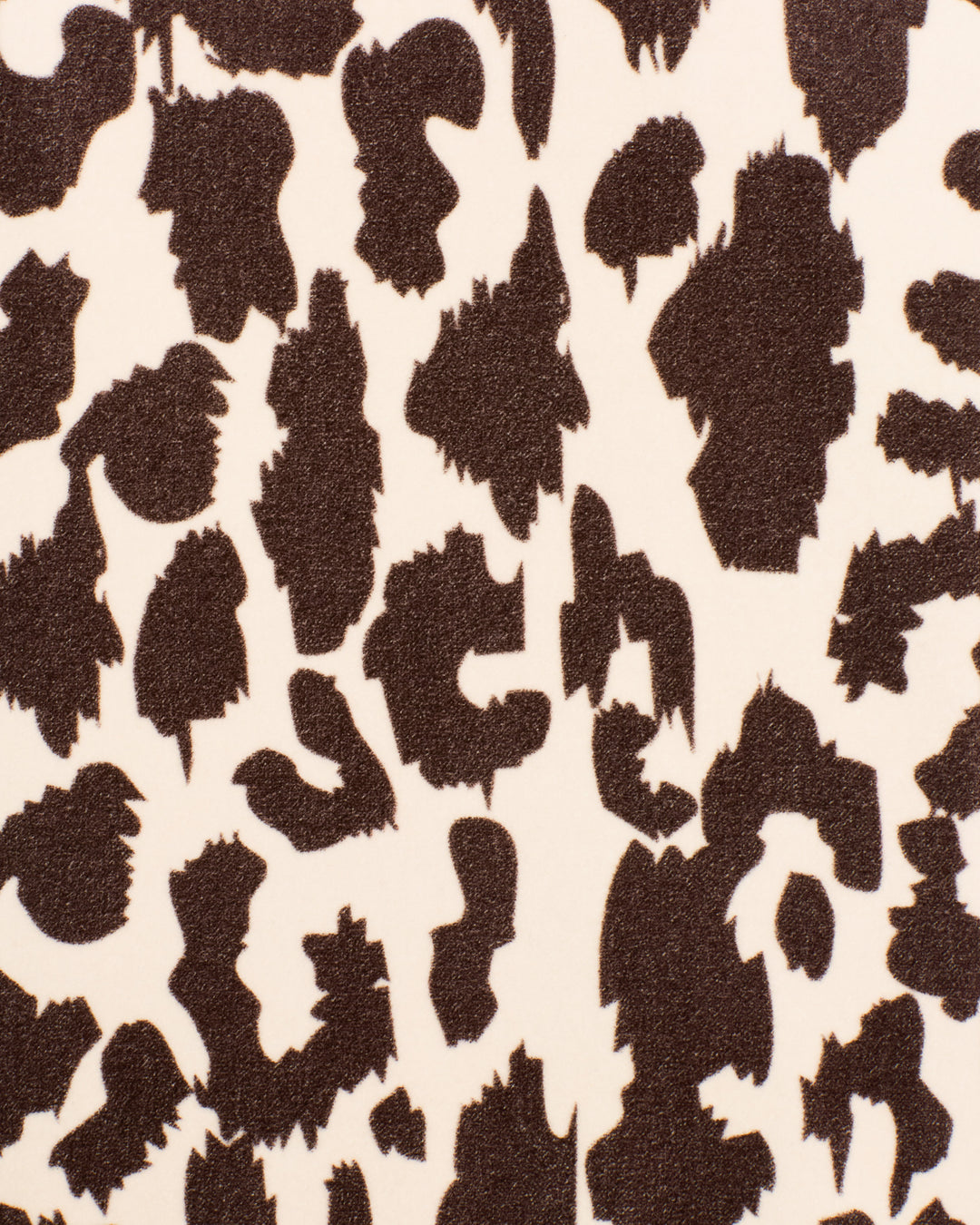 Close-up of the Lydia Leopard Steppe Jacket’s fabric, showcasing an irregular black and brown leopard print on a light beige background, reminiscent of vintage patterns often found on classic cotton-velvet outerwear.