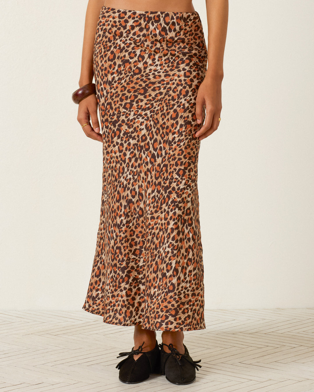Wearing the Lyra Leopard Trek Silk Skirt, paired with black shoes and a brown bangle, the person stands against a plain background.