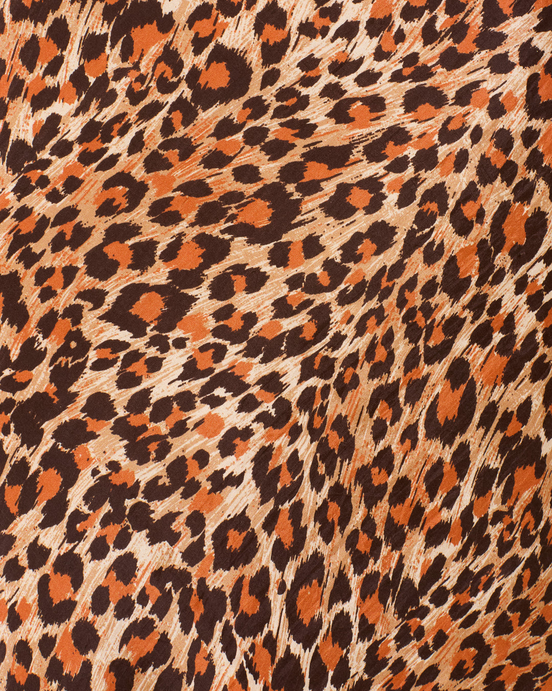 Close-up of a leopard print pattern, showing irregular black and orange spots on a light brown background, reminiscent of the bold design featured on our Lyra Leopard Trek Silk Skirt.
