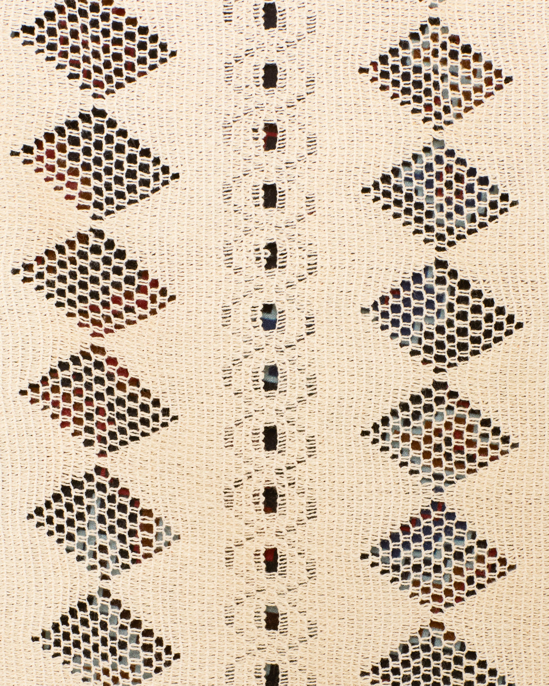 Close-up of the Marcie Savanna Lattice Dress, featuring cream-colored crochet fabric adorned with diamond-shaped patterns and a vertical row of square openings at the center. Multicolored threads peek through the openwork, showcasing intricate details reminiscent of geometric lace and bohemian style.