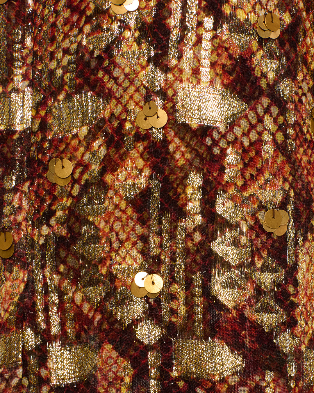 Close-up of the Nia Topaz Snakeskin Dress, showcasing textured fabric with a red and gold geometric pattern accented by shiny gold sequins scattered across the surface, evoking the opulent effect of luxurious gold fil-coupé details.
