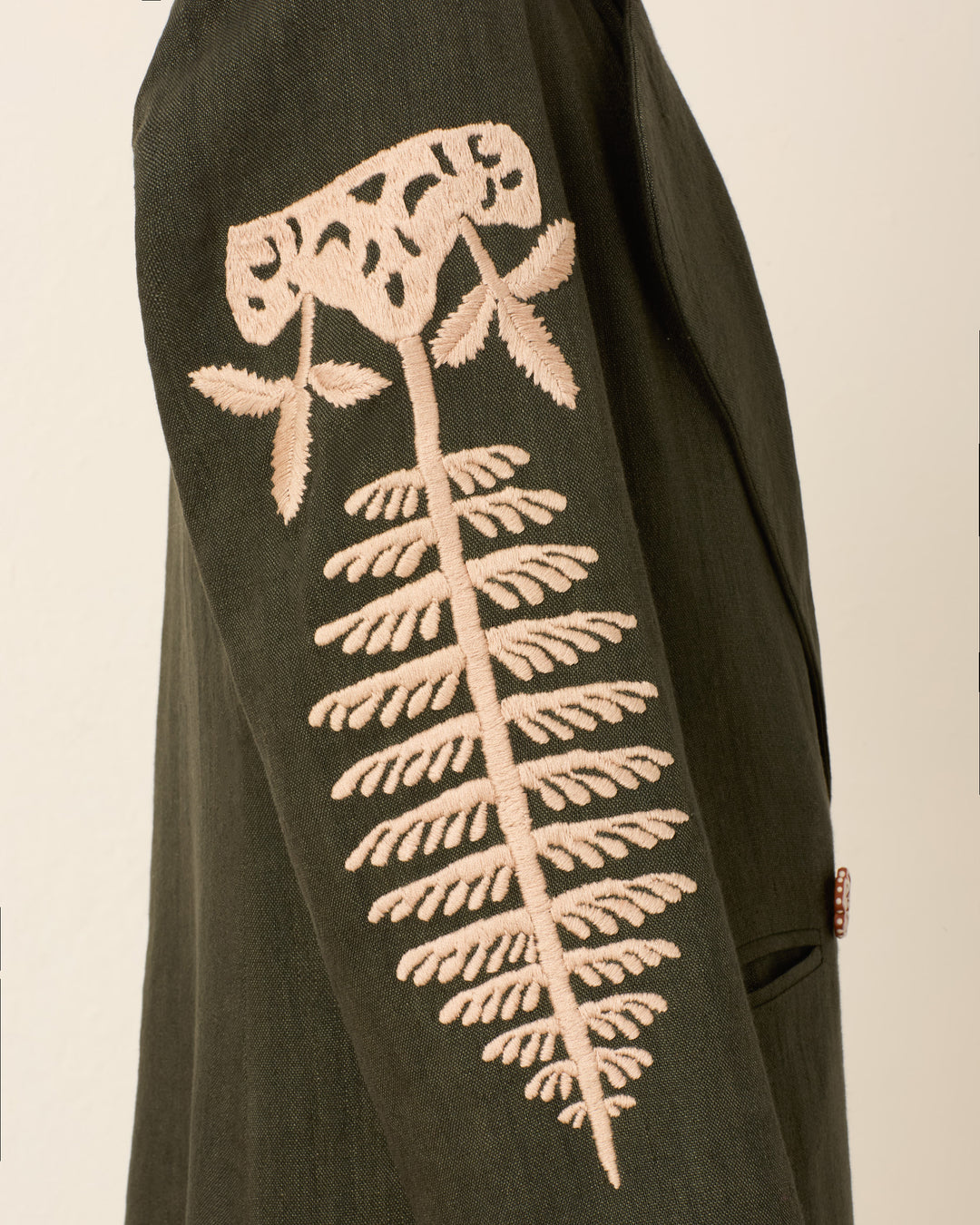 A close-up of the Petunia Grassland Fern Coat’s dark green sleeve highlights the beige hand-embroidered fern and flower design, complemented by an Italian wool fleece collar.