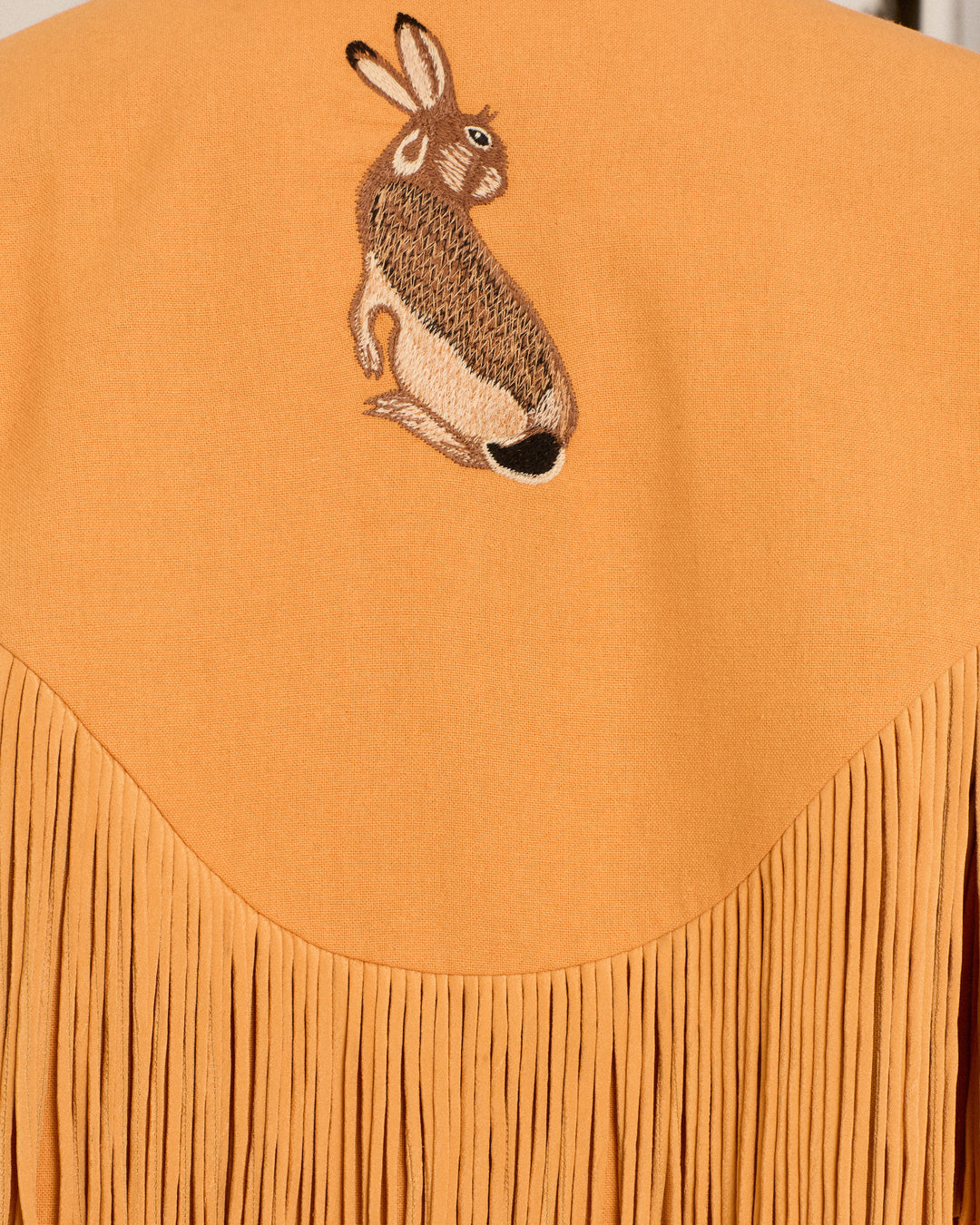 The Ranger Sunset Hare Jacket is hand-embroidered from tan Italian wool fleece, featuring long fringe and a charming embroidered rabbit on the upper back—a playful detail that highlights luxurious craftsmanship.