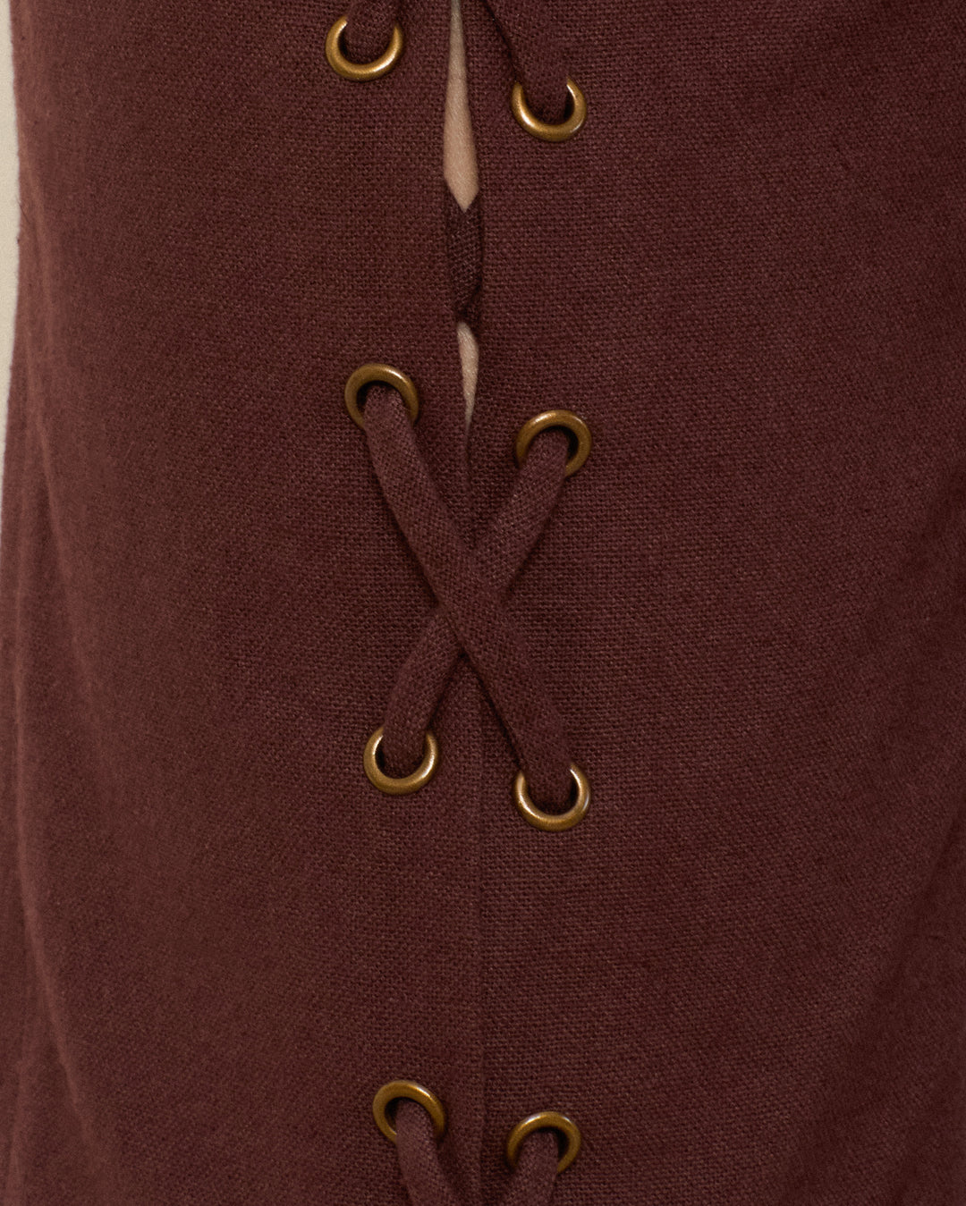 Close-up of the Razza Mahogany Pant featuring brown fabric with grommeted lace-up ties threaded through gold eyelets, partially revealing a light background beneath the laces.