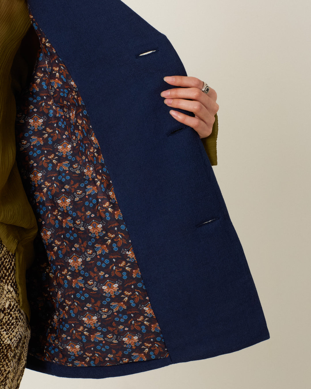 A person holds open the Rivoli Midnight Mischief Coat, revealing its brown floral-patterned lining. Only their hand, part of their arm, and the coat are visible.