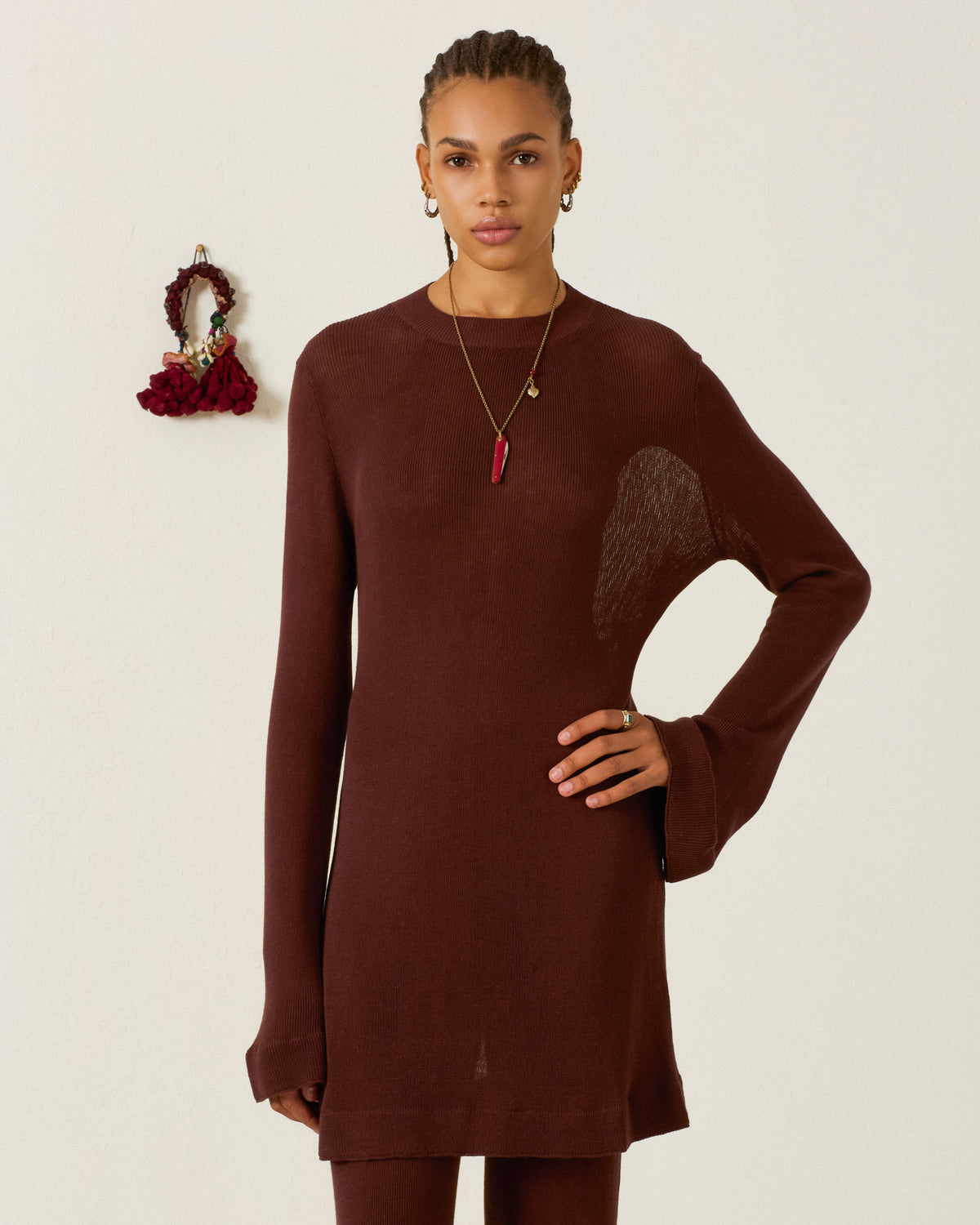 A person wearing a long-sleeved, brown bamboo viscose Romy Mahogany Knit Dress with flared sleeves and a pendant necklace.