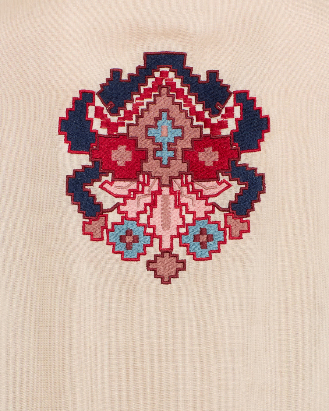 Geometric, symmetrical kilim motifs are hand-embroidered in red, blue, and brown thread on a beige fabric background, creating a striking accent for the Rune Kilim Stone Fringe Top.