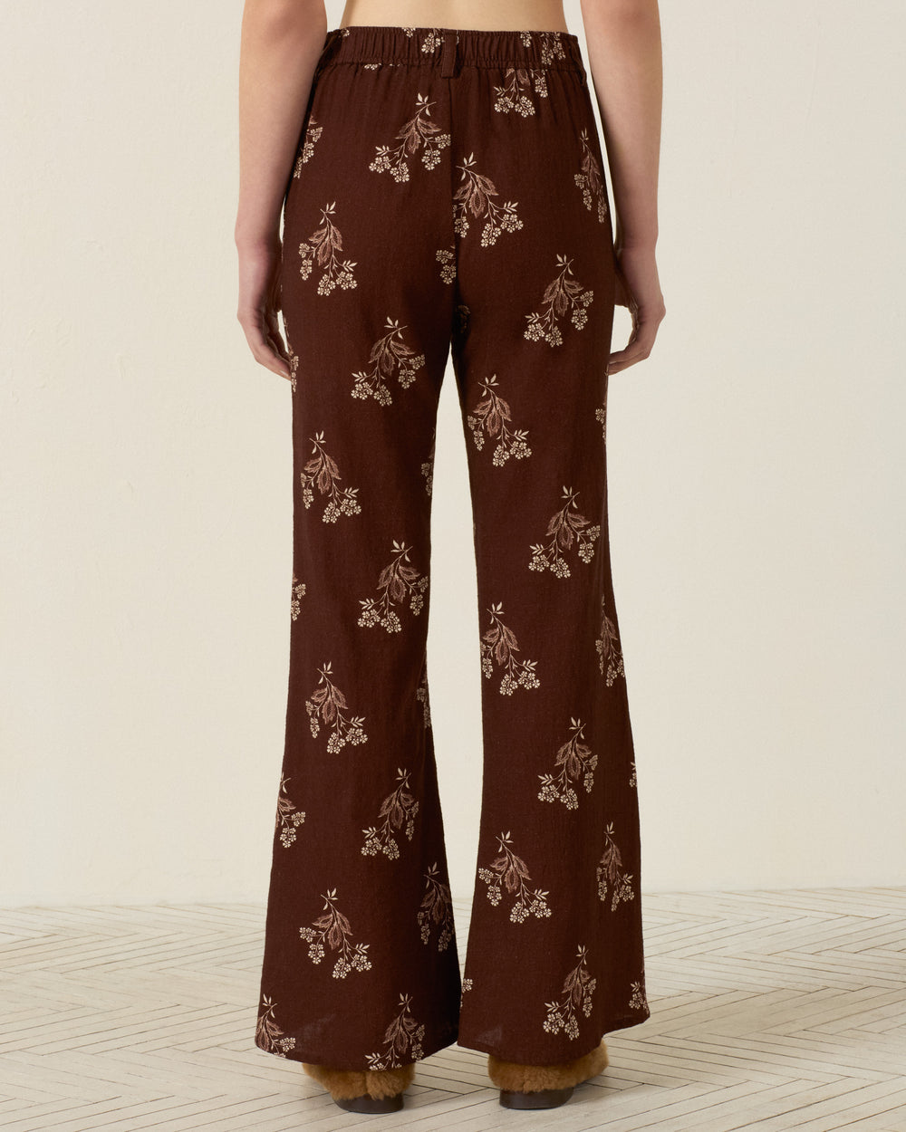 Person wearing the Sonnet Doe Elderflower Jean, a high-waisted, wide-leg cotton pant with a floral print, shown from the back while standing on a light-colored floor.