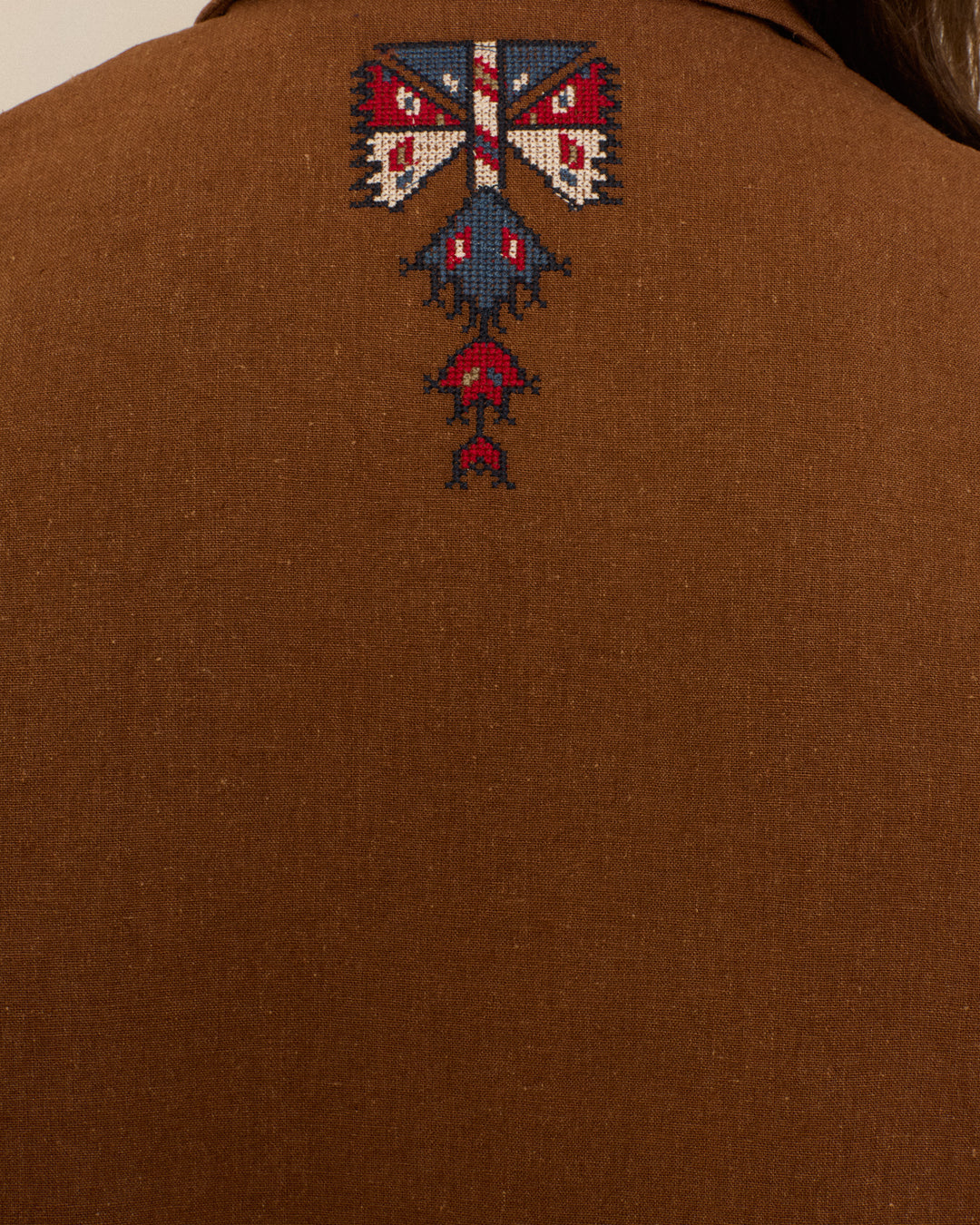 Close-up of the back of the Western Doe Arrow Silk Jacket, an exquisite artisan garment featuring an intricate hand embroidery pattern in red, blue, white, and black near the collar.