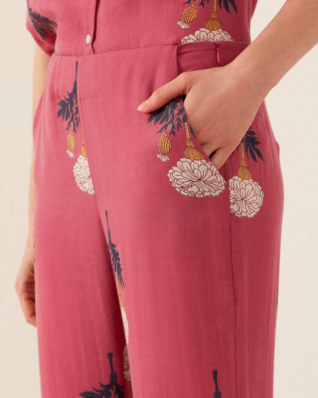 A person wearing the Charlie Hibiscus Rose Pant, adorned with retro floral patterns, stands with one hand in their pocket. The fabric exudes a vintage feel, showcasing dark and light floral designs in shades of white, yellow, and navy blue.