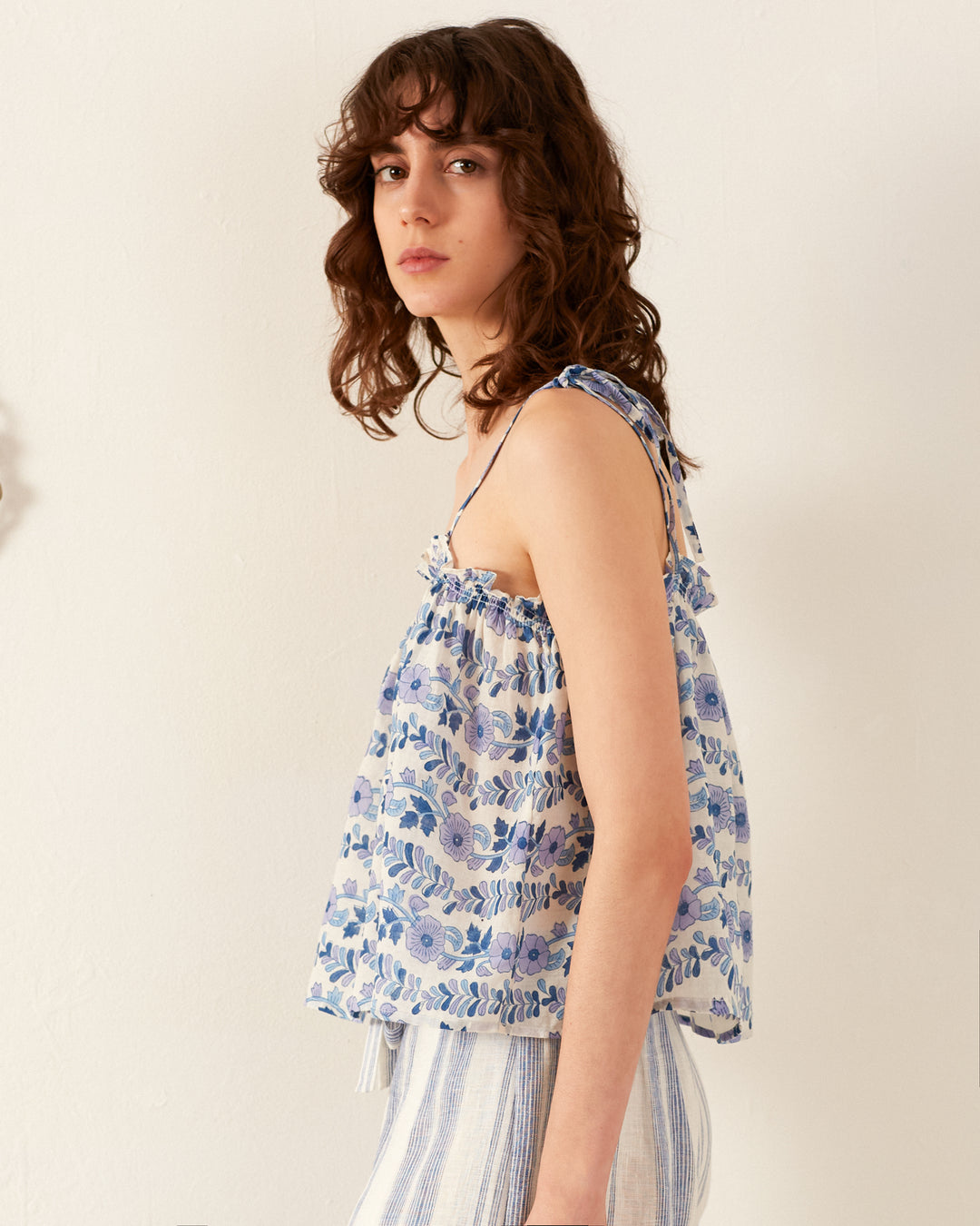 A person with wavy brown hair is wearing the Lila Iris Ivy Top and striped pants, standing against a plain light background. They are looking at the camera with a neutral expression.