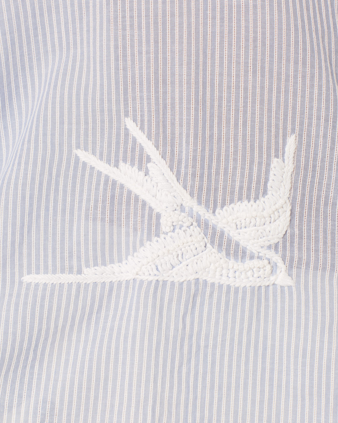 Close-up of the white embroidered bird design on the Emery Swallow Stripe Shirt, a hand-embroidered cotton shirt with light blue and white vertical stripes.