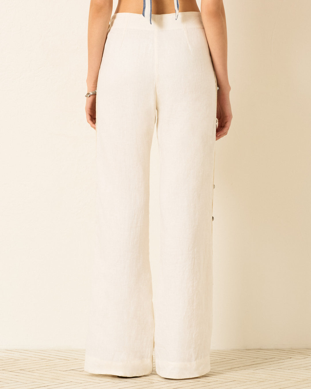 A person is shown from the waist down wearing the Holland Pearl Linen Pant—high-waisted, wide-leg sailor pants with silver buttons made of lightweight fabric—standing against a plain background.