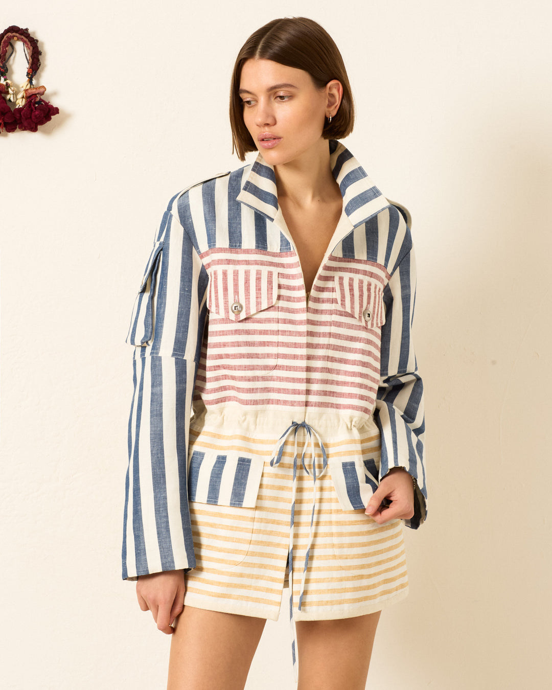 A woman wears the Porter Sailor Stripe Jacket—with blue, pink, and yellow stripes—paired with matching shorts, standing against an off-white wall.