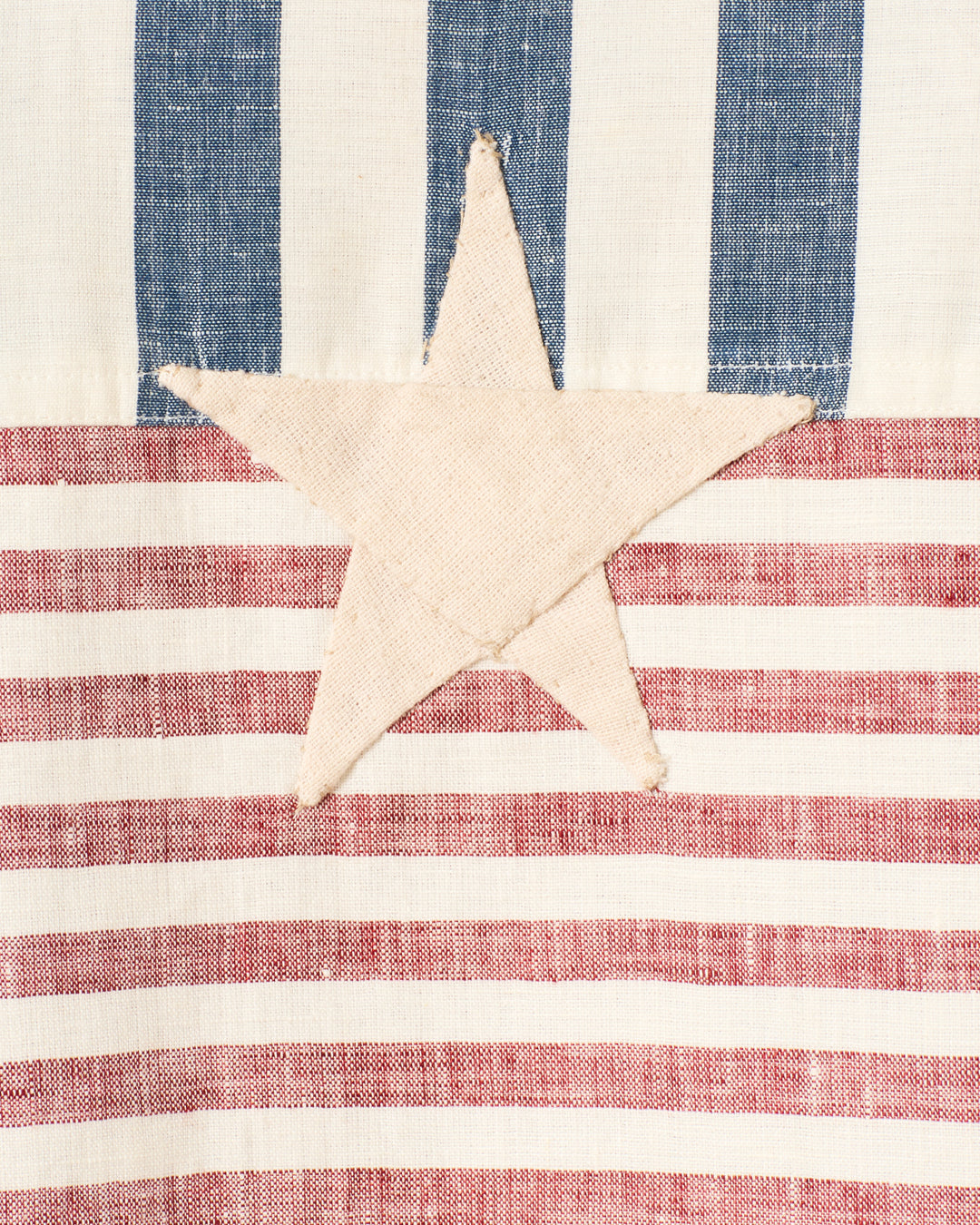 The Porter Sailor Stripe Jacket features a beige handmade star appliqué on blue vertical and red horizontal stripes, evoking elements of the American flag.