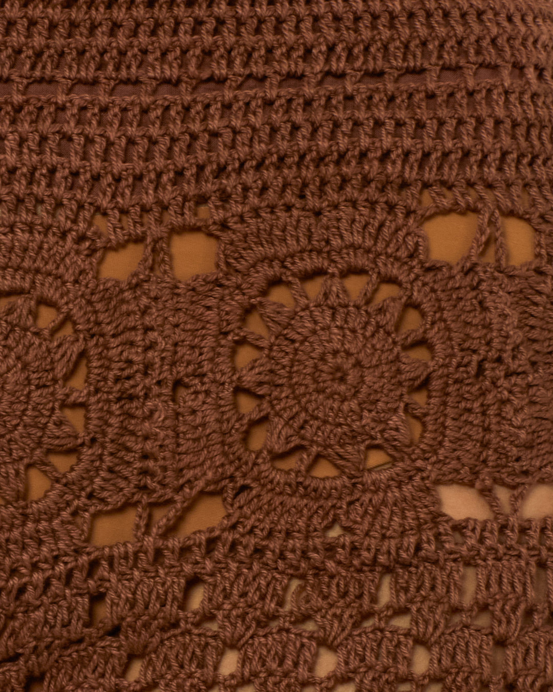 Close-up of Aletta Clove Mandala Pant—artisan crochet pants with brown hand-crocheted fabric, circular and geometric patterns, small gaps, and a tan background. Perfect as a unique crochet swimwear cover-up.