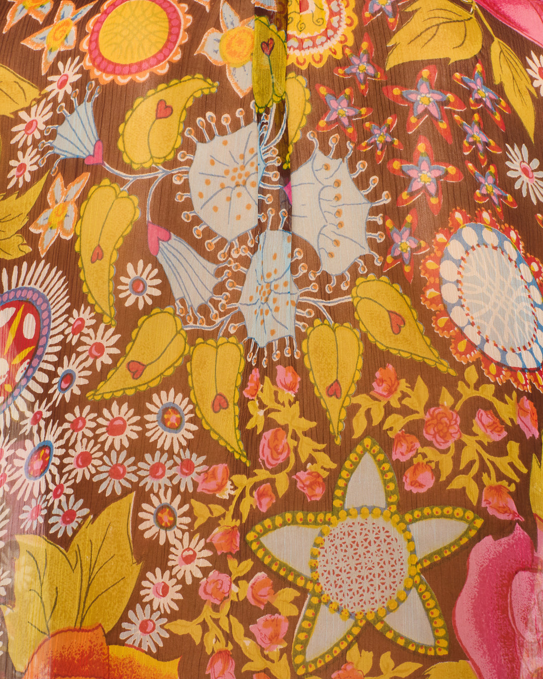 A close-up of the Annabel Bloom Mirage Shirt, featuring colorful, vintage-inspired psychedelic floral and geometric patterns in yellow, pink, blue, and white on a brown background.