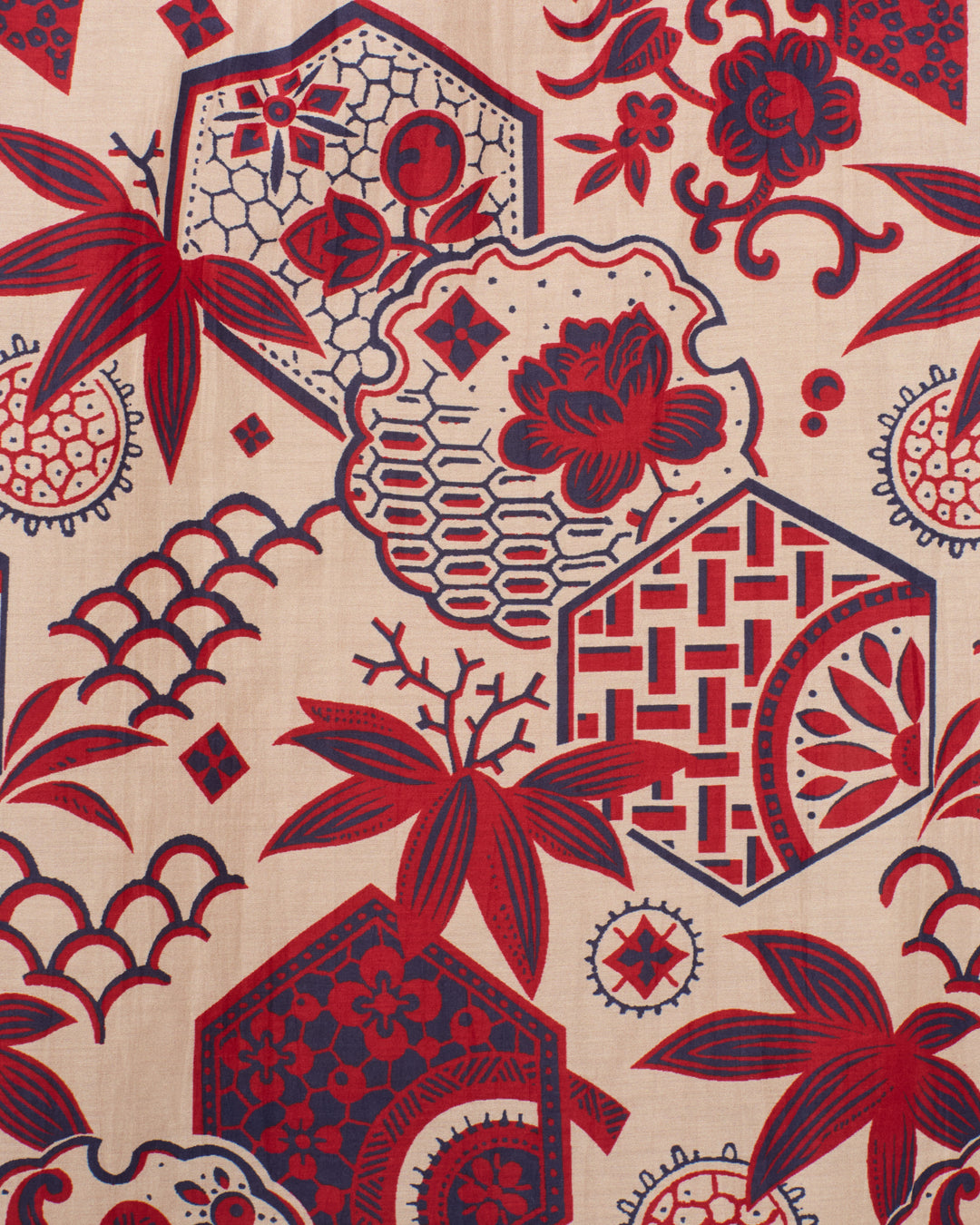 The Annabel Crimson Hive Shirt features beige fabric adorned with repeating red and navy blue botanical motifs, hexagons, and geometric patterns inspired by traditional wagara prints.