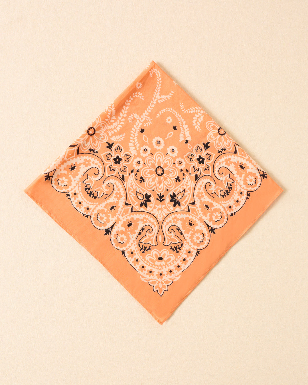 The Bodhi August Bandana, in a peach cotton-silk blend with a white and black botanical motif, is displayed flat on a light beige surface.