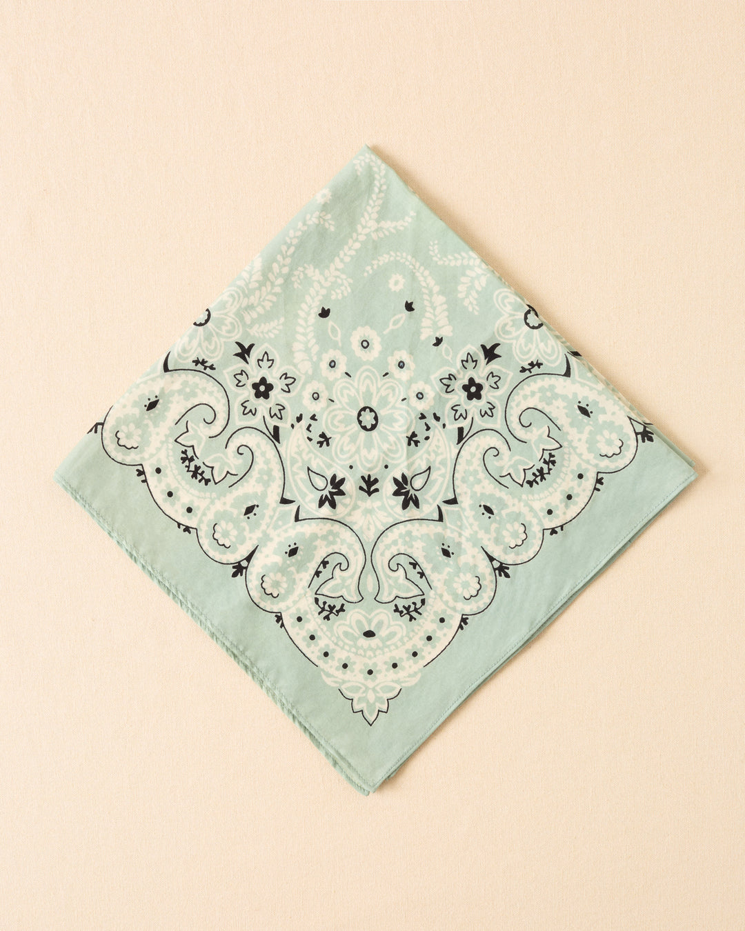 The Bodhi Searise Bandana is a light green cotton-silk accessory featuring a black and white floral and paisley motif, displayed flat against a beige background.