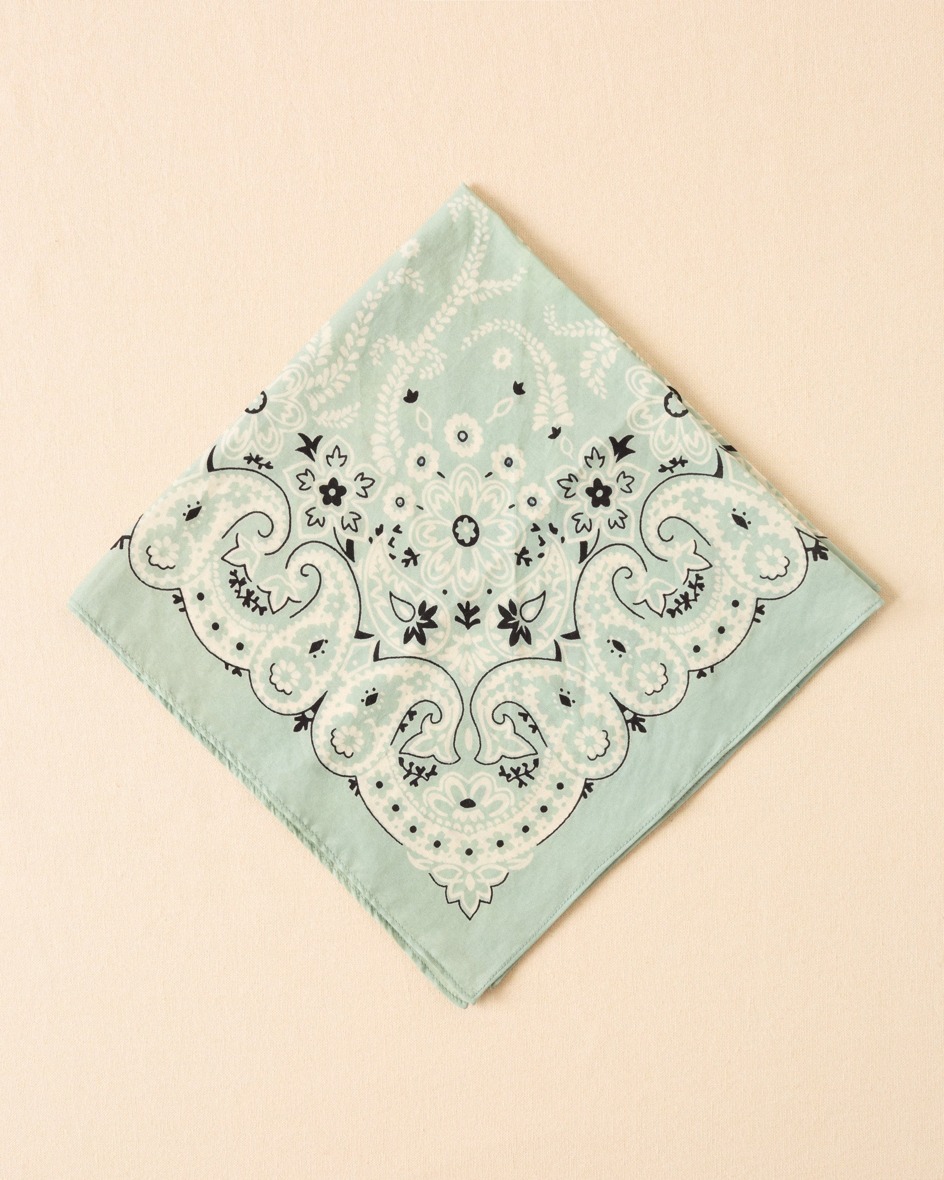 The Bodhi Searise Bandana is a light green cotton-silk accessory featuring a black and white floral and paisley motif, displayed flat against a beige background.