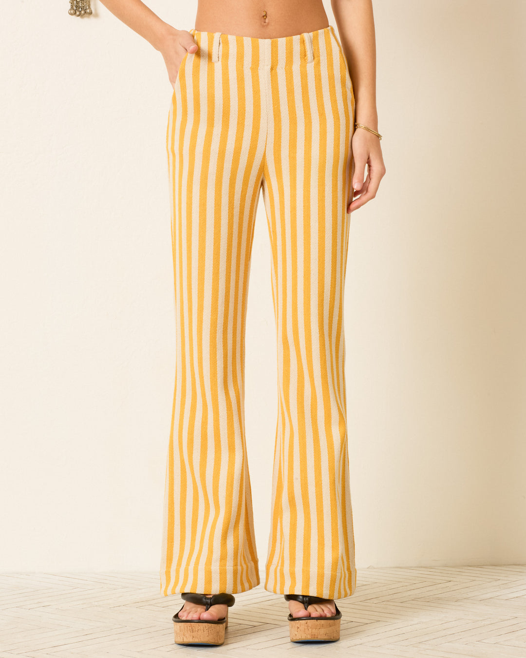 A person wearing the Charlie Sunlight Stripe Pant—high-waisted, yellow and white striped cotton twill flared pants—and black platform sandals, standing against a light background.