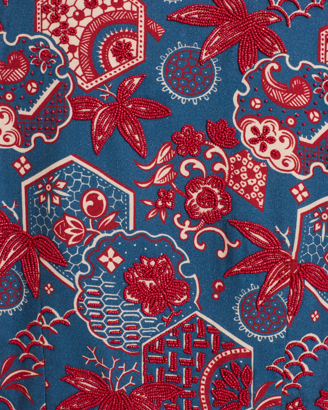 The Clarke Delft Hive Jacket is crafted from blue Khadi cotton fabric with red and white floral and geometric patterns—hexagons, circles, stylized flowers and leaves—and finished with handmade floral buttons for a unique touch.