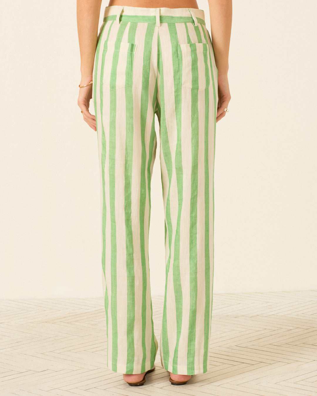 A person is seen from the back standing on a patterned floor with a light-colored background, wearing the Colette Celery Stripe Pant in a relaxed silhouette.