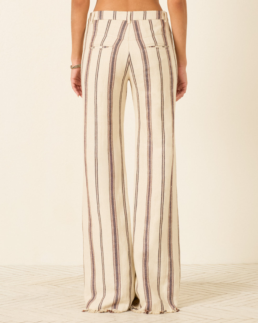 Wearing the Cooper Bark Stripe Pant—high-waisted, flared trousers with vertical beige and brown stripes in a linen-cotton blend—photographed from the back against a neutral background.