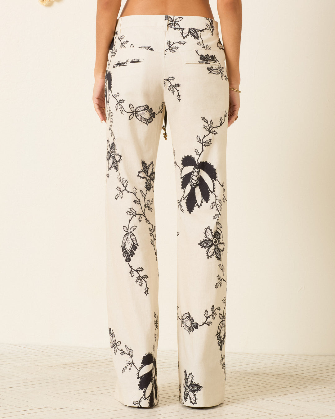 Person standing with their back to the camera, wearing Cooper Shadow Lace Pant—high-waisted Khadi cotton pants with a black floral print and stylish flared leg.