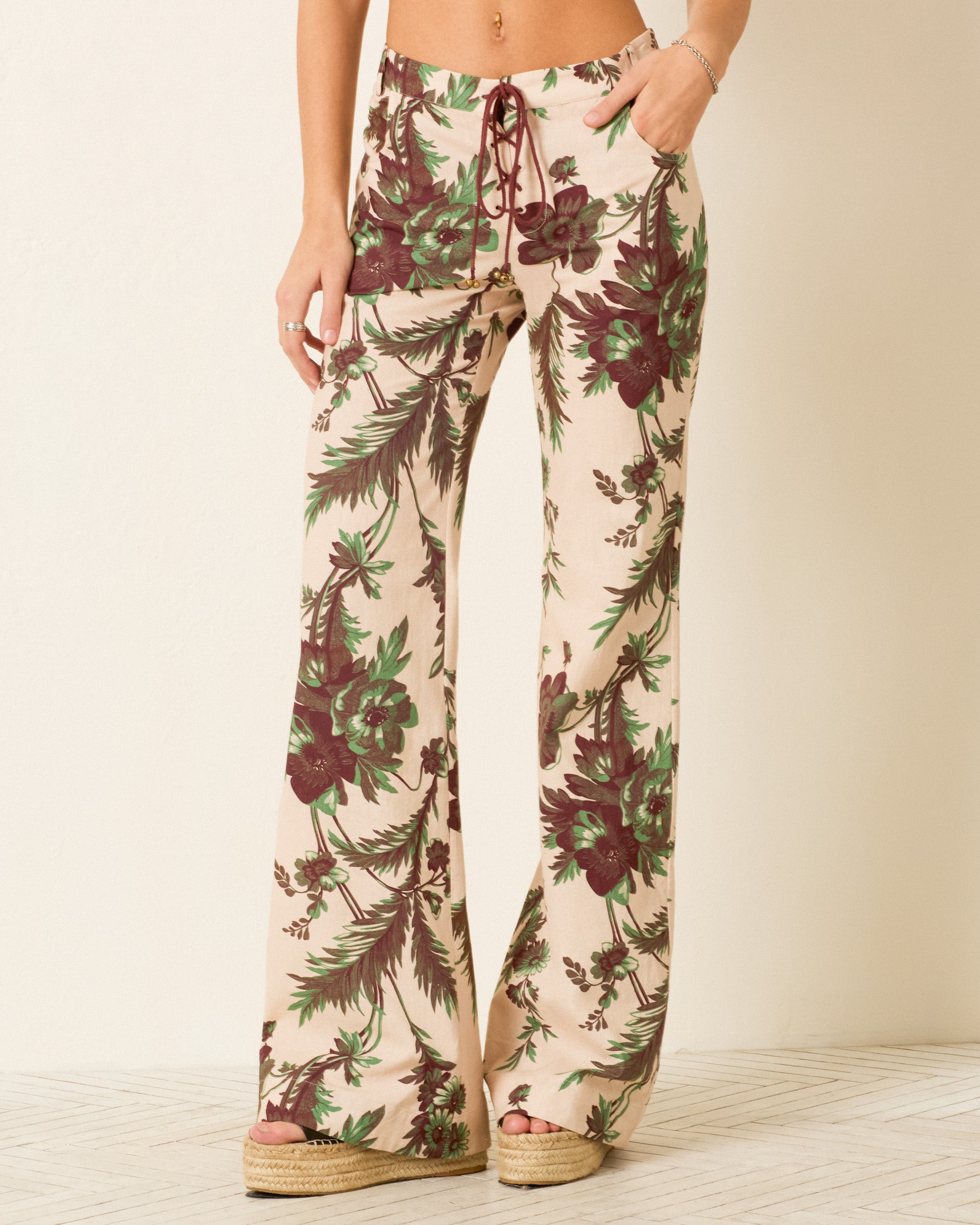 A person wearing the Cooper Summermoss Pant—cream-colored khadi cotton with a green and maroon botanical motif, wide legs, and lace-up front—paired with platform espadrille sandals.