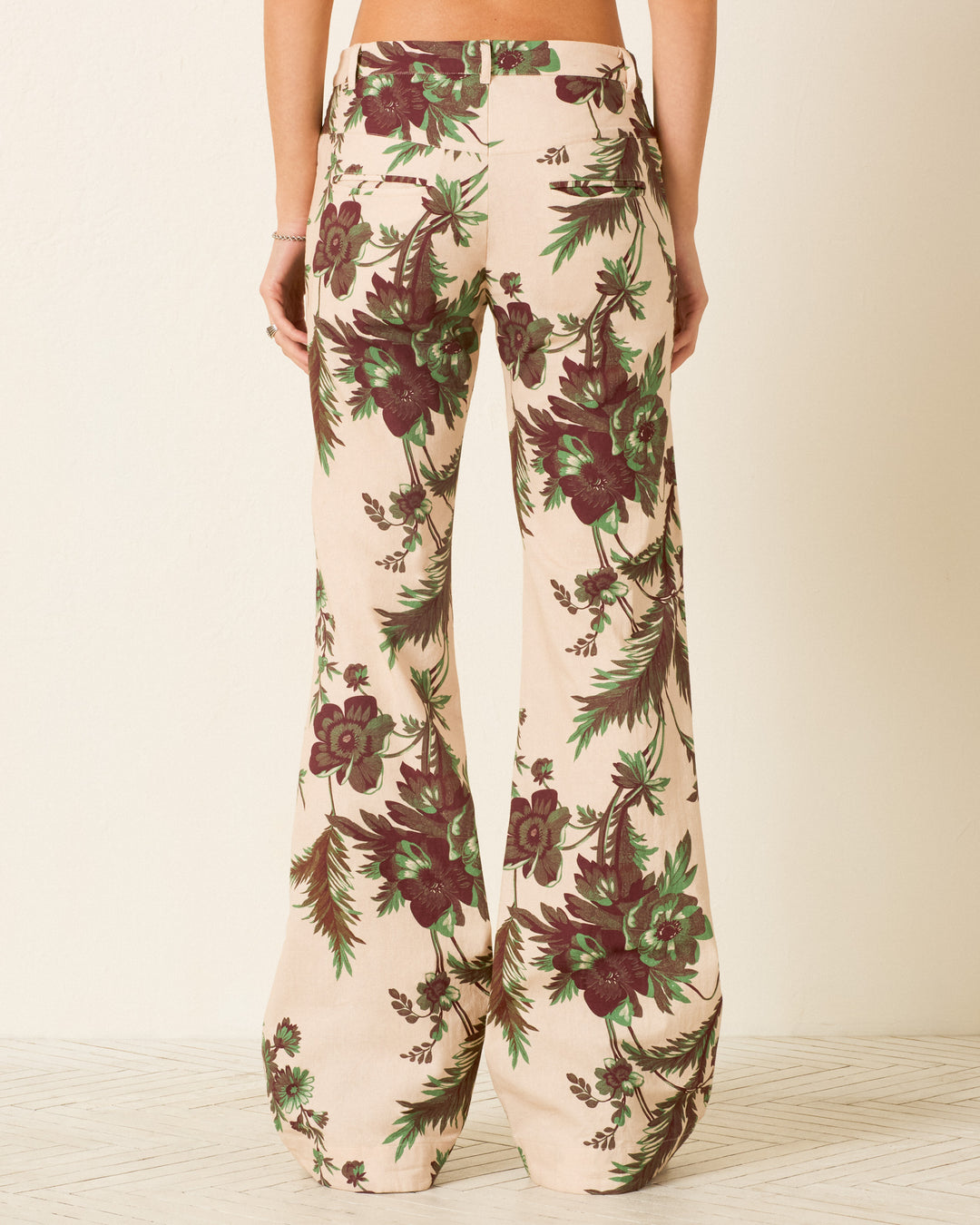 A person wearing Cooper Summermoss Pant in beige Khadi cotton with green and maroon botanical motifs, seen from the back against a plain light-colored wall.