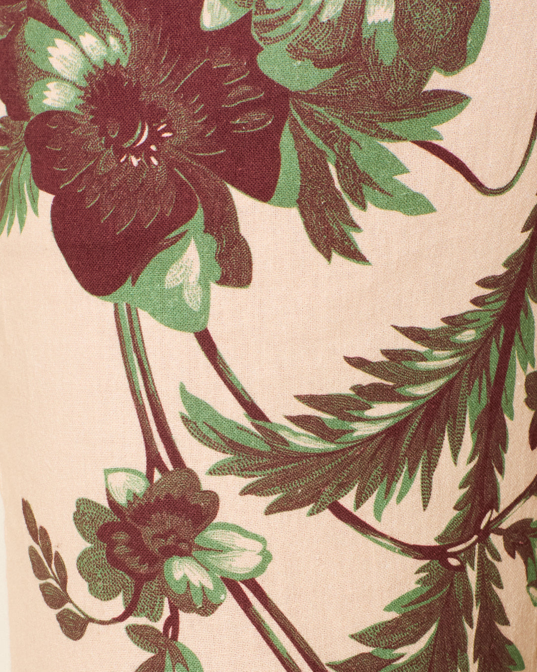 Close-up of the Cooper Summermoss Pant, crafted from Khadi cotton with a botanical design of large maroon flowers and green leaves on a light beige background.