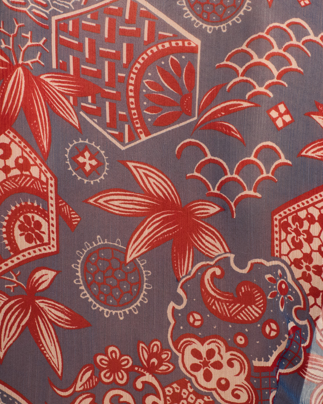 The Dana Delft Hive Shirt showcases red and white floral and geometric patterns on a blue cupro-chiffon background, featuring stylized flowers, leaves, and lattice designs.