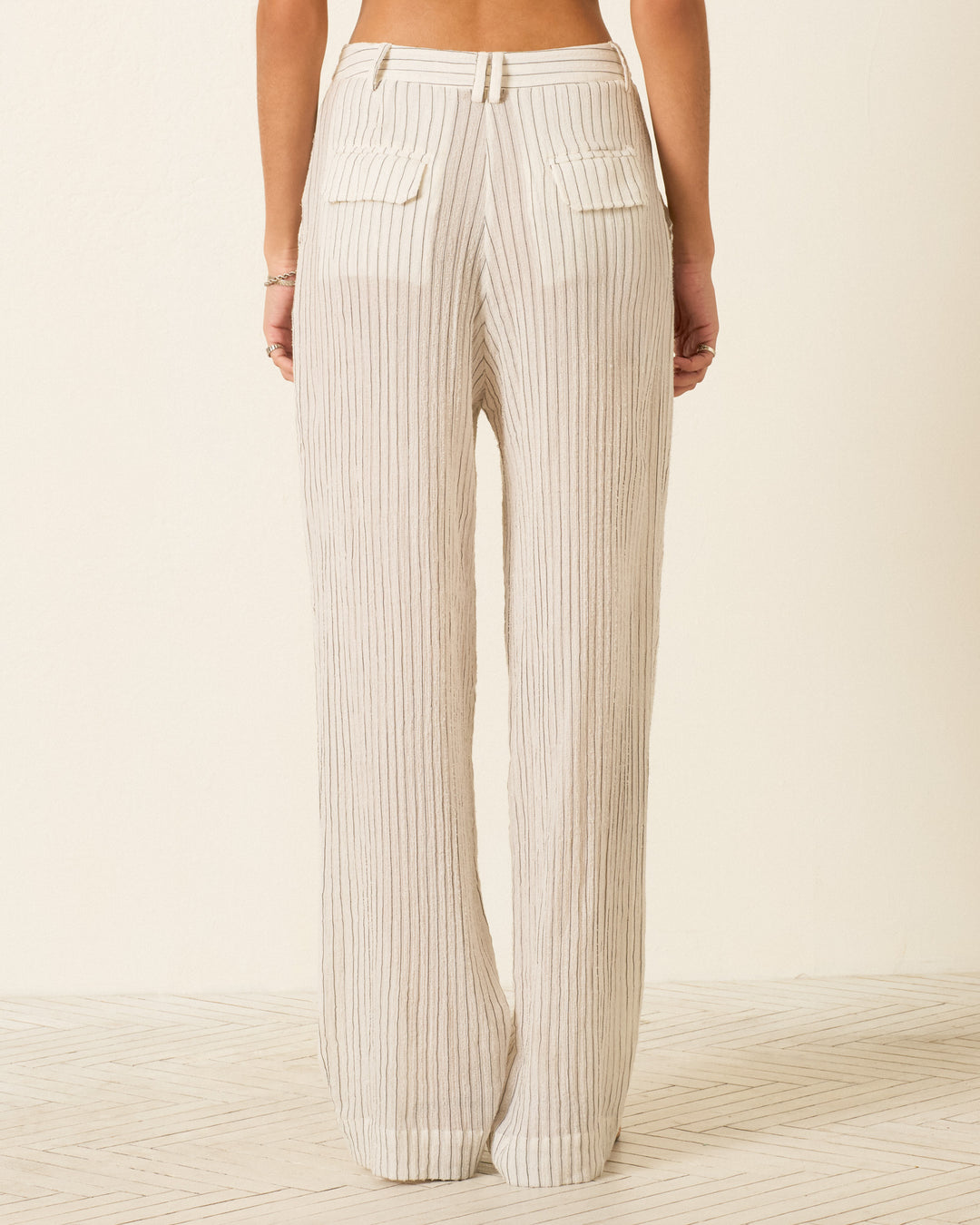 A woman wears the Diana Sea Salt Pant—high-waisted, wide-leg, relaxed fit ribbed beige pants with back pockets—shown from the rear against a neutral background.