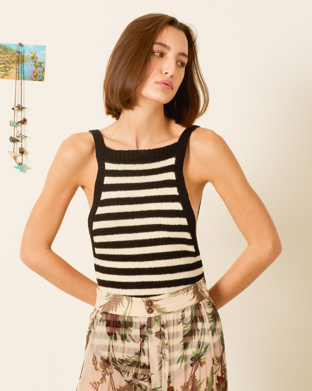 A woman wearing the Etta Tuxedo Stripe Bodysuit stands with her hands on her hips against a light-colored wall.